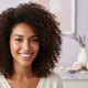 Close-up portrait of a smiling young woman with perfectly styled, bouncy curls, looking confident and happy.